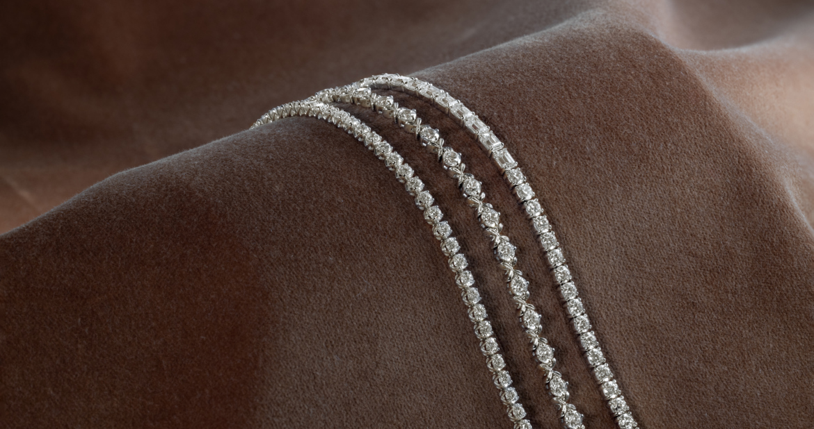 Three diamond tennis bracelets with different link styles displayed on brown fabric.