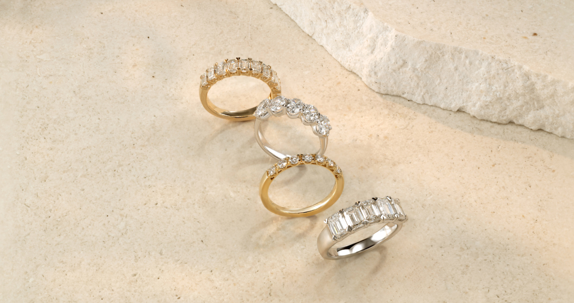 "Four diamond wedding bands in gold and platinum with different stone cuts and settings on marble surface.