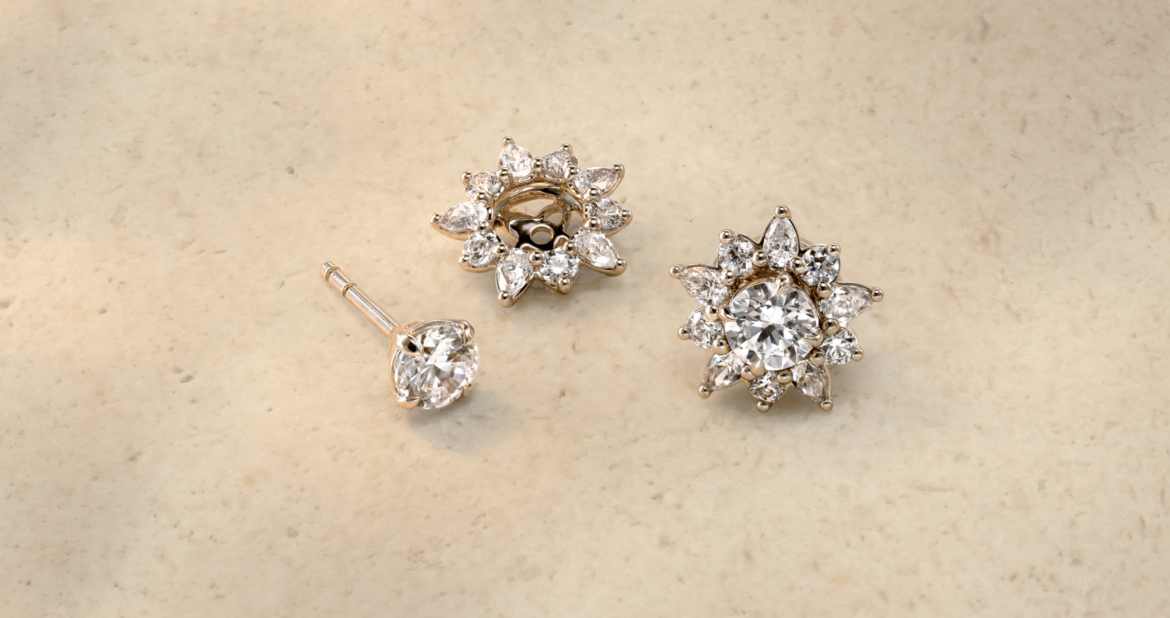 Diamond stud earrings and matching flower-shaped diamond earring jackets on marble surface.