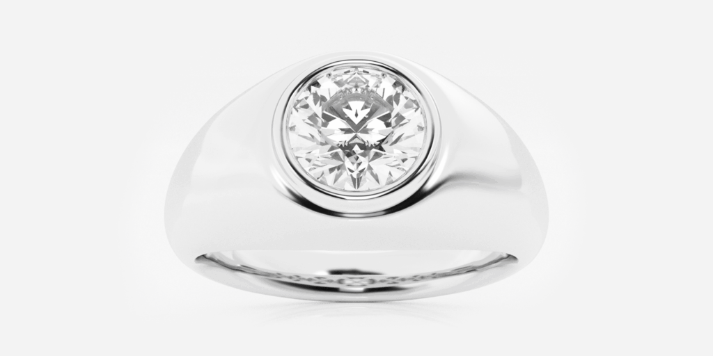 A white gold or platinum signet ring featuring a large round brilliant-cut diamond set in a bezel setting, with a smooth polished band, displayed against a white background.